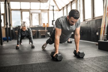 fit people doing dumbbell push-ups at the gym