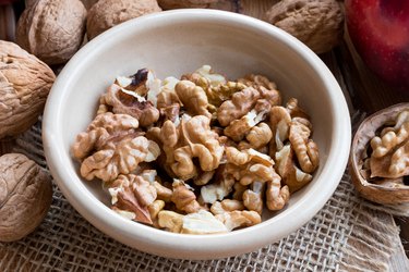 Shelled walnuts in a bowl, with whole walnuts and an apple