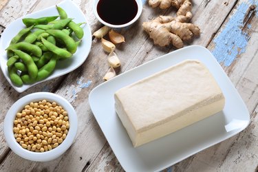 Tofu block, edamame and soybeans and soy sauce on wooden table