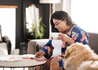 a person wearing a floral shirt writes in a journal at home, as a form of self-care