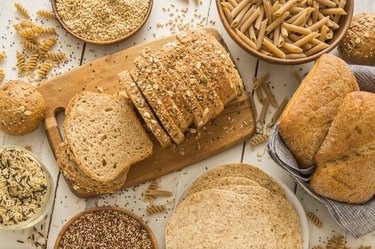 Starchy foods including pasta and brown bread on cutting board