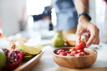 man's hand reaching for strawberries in bowl