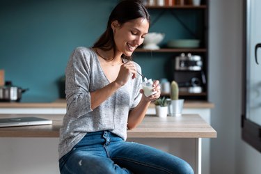 Smiling young woman sitting in her kitchen eating yogurt, as a natural remedy for a yeast infection