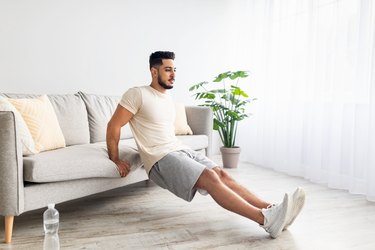 Person doing triceps dips in living room using couch as part of a 15-minute upper-body workout.