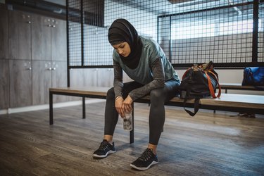 Person sitting on bench in gym looking tired.