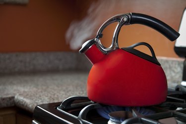 Shiny Red Tea kettle on gas stovetop with smoke coming out of the spout.