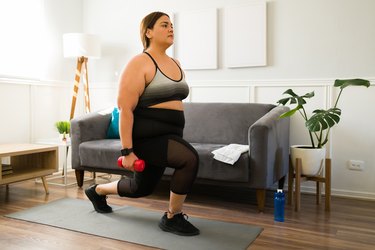 Person doing a dumbbell lunge in their living room to strengthen their glutes