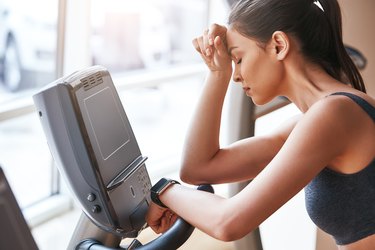 Feeling tired. Side view of young woman in sports clothing keeping hand on forehead while exercising at gym