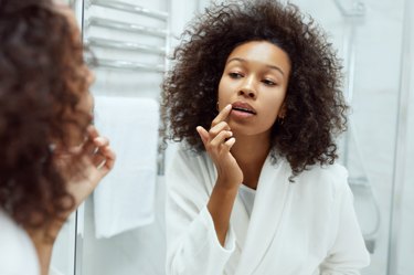 Woman looking in the bathroom mirror and applying a cold sore patch, as a cold sore remedy