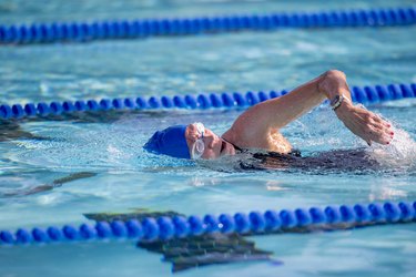 Athlete with blue cap and dark one-piece bathing suit swimming in pool