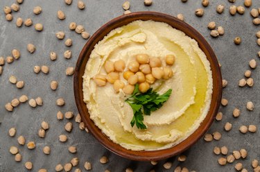 Flat lay view at hummus topped with green coriander leaves on stone table covered with chickpeas