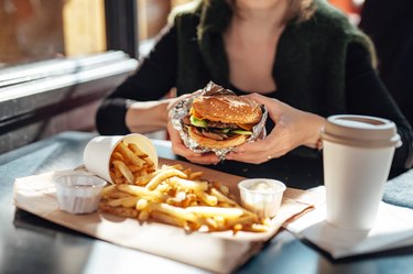 Person holding a freshly served cheeseburger in an outdoor cafe