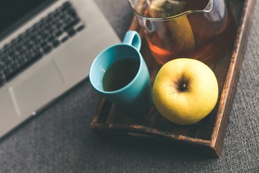 Close-Up Of Coffee And Apple for Energy in a Tray Next to Laptop