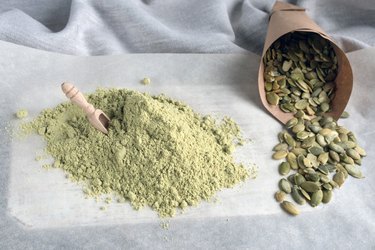 Wooden scoop in flour with pumpkin seeds on a white background.