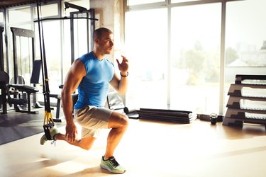 Man doing leg exercises with suspension straps at gym.