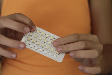 a close up photo of a person wearing an orange tank top holding a packet of birth control pills