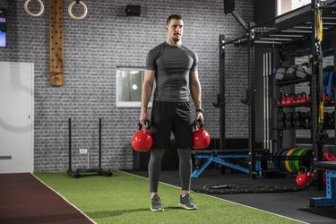 caucasian man doing the kettlebell farmer's walk exercise with two kettlebells in the gym