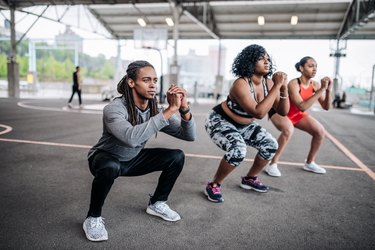 Three people wearing workout clothes performing squats outside.