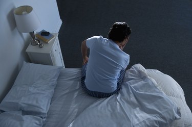 back view of a man sitting up in bed because of heart palpitations at night