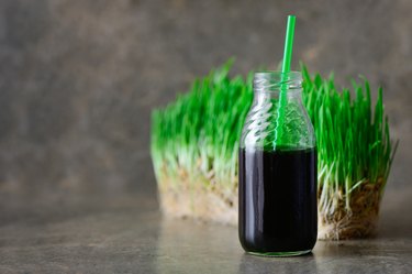 A bottle of liquid chlorophyll with a straw in front of a slab of wheatgrass