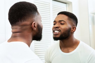 Young black man looking at his bleeding gums in the bathroom mirror