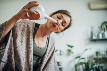 A woman using a neti pot, as a home remedy for allergies