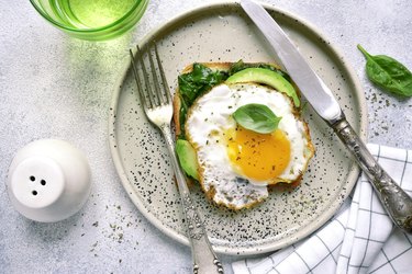 overhead photo of avocado slices, sauteed spinach and fried egg on toast with fork and knife