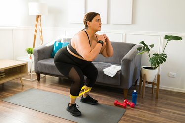 Person wearing black sports bra and leggings doing a resistance band squat in living room.
