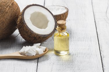 Glass bottle of coconut oil with fresh coconut fruit on rustic background, alternative theraphy medicine concept, Cocos nucifera