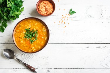 Vibrant bowl of thiamin-rich red lentil soup sits on a white wooden table with fresh cilantro.