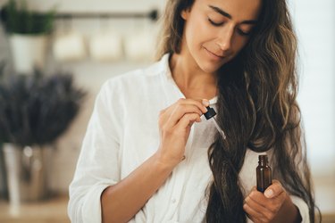 Young person with long brown hair applying germ wheat oil for skin lightening and squalene for hair