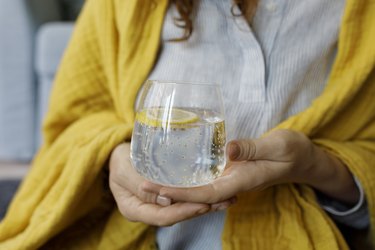 Hands of a person holding a glass of sparkling water with a lemon slice