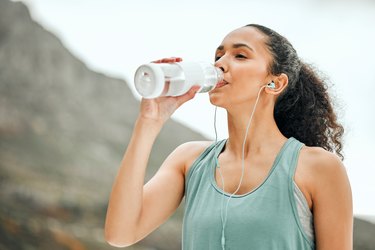 a person with brown curly hair in a ponytail drinking from a reusable water bottle during a workout, as a natural remedy for asthma