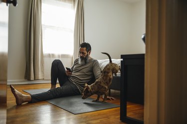 Mature man sitting on bedroom floor looking at smart phone