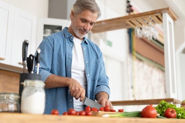 Grey-haired Mature handsome man preparing delicious and healthy food in the home kitchen.