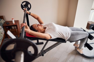 woman doing a barbell bench press in her home