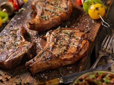 Tender grilled barbecue pork steaks on a wooden cutting board with vegetable skewers.