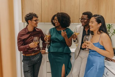 Four young people in kitchen drinking alcohol and smiling can lead to alcoholic swollen fingers