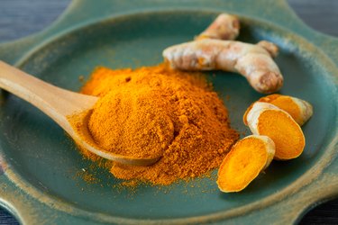 Turmeric powder and root with wooden spoon on teal plate