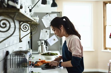 Person in a blue and pink sweater and ponytail chopping vegetables at their kitchen counter to eat them for better thyroid health