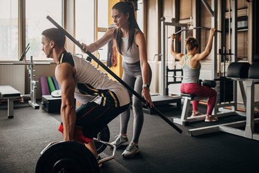 Personal trainer holding a dowel to the back of a man deadlifting to show common deadlift mistakes and proper form