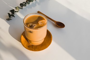 Coffee with ice in a crystal glass on the white table in natural light