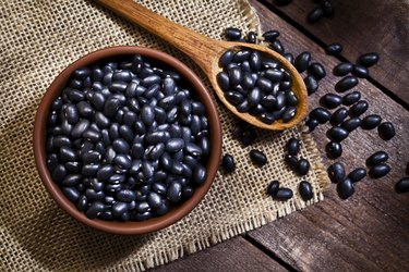Tyrosine-rich black beans in a wooden bowl and wooden spoon on a brown background
