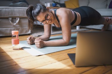 woman wearing glasses doing Pilates workout video at home with laptop and water bottle