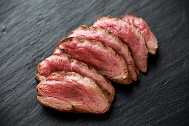 Medium rare venison steak on rustic dark stone board