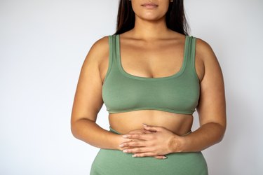 a person wearing a green bra and leggings with long straight hair holding their stomach