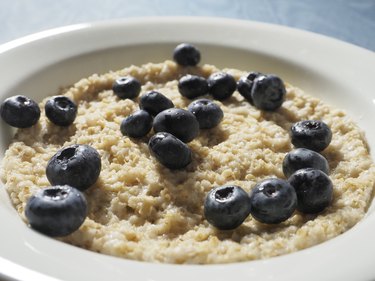 a close up of a white bowl of creamy oatmeal topped with blueberries