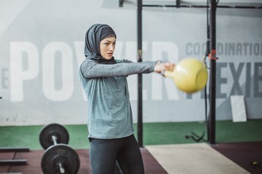 Person wearing hijab performing kettlebell swing in gym