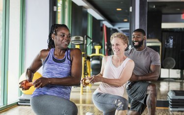 Three people in a gym doing the wood chop exercise with a dumbbell.