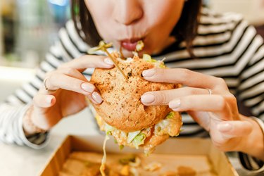 close view of a person eating a hamburger, to represent stomach pain from greasy food